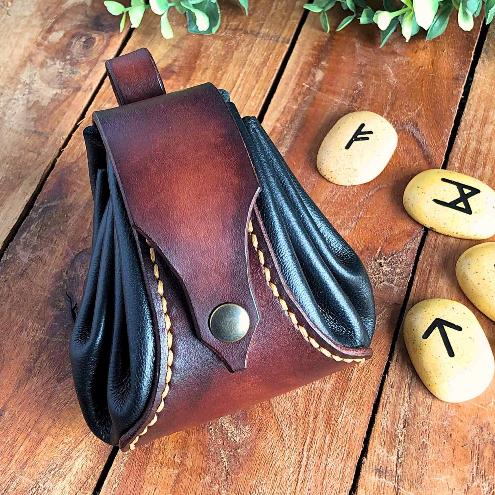 Brown leather drawstring dice pouch with black sides on a wooden surface with rune stones.