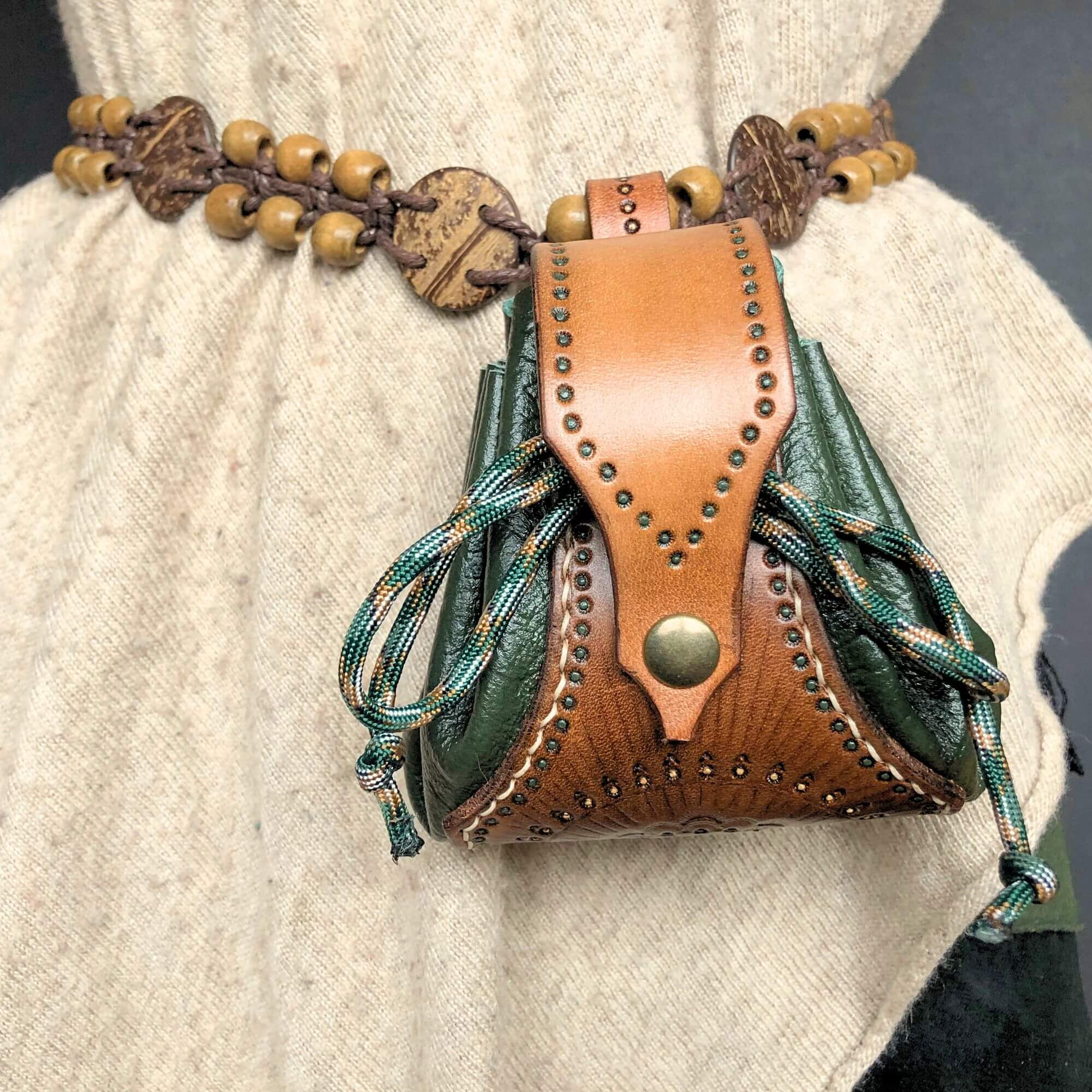 Handmade leather drawstring pouch with decorative elements on a person wearing a light-colored garment.