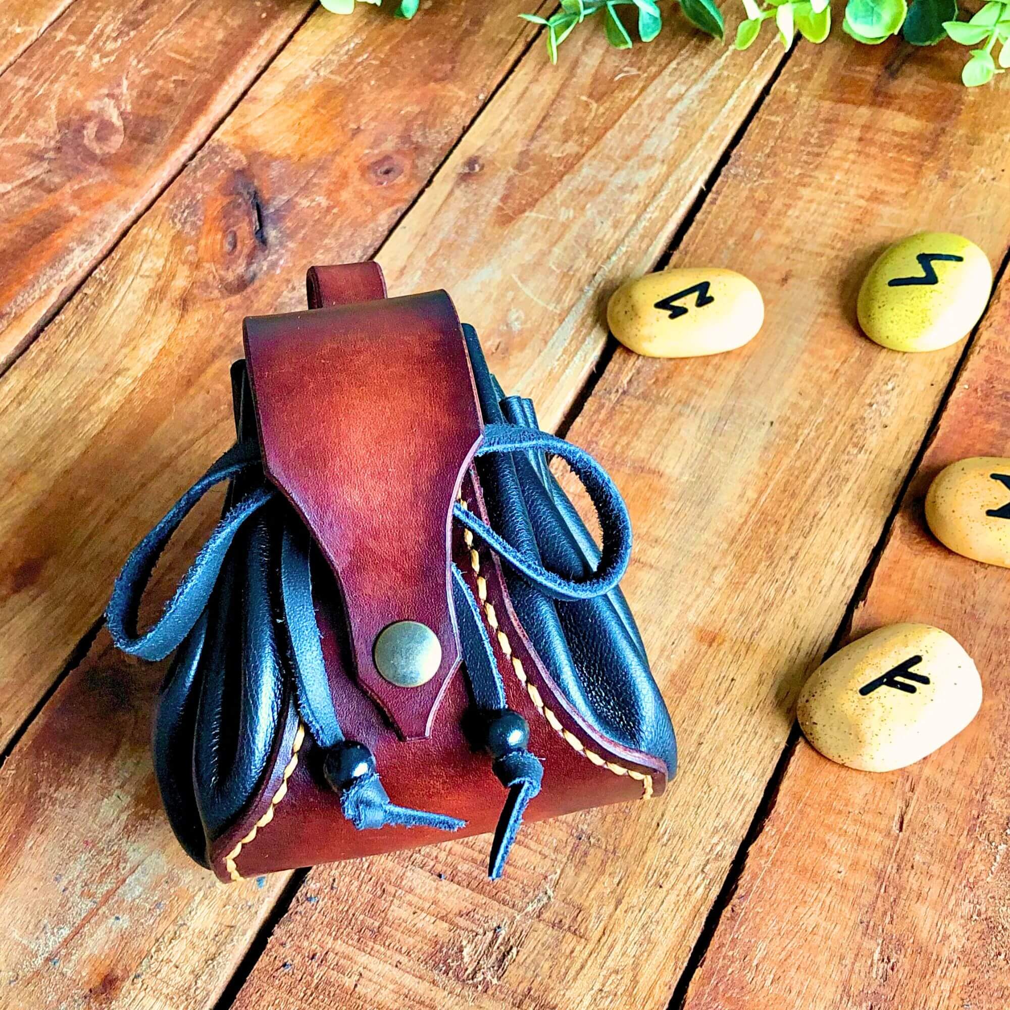 Drawstring leather pouch with rune stones next to it on a wooden background