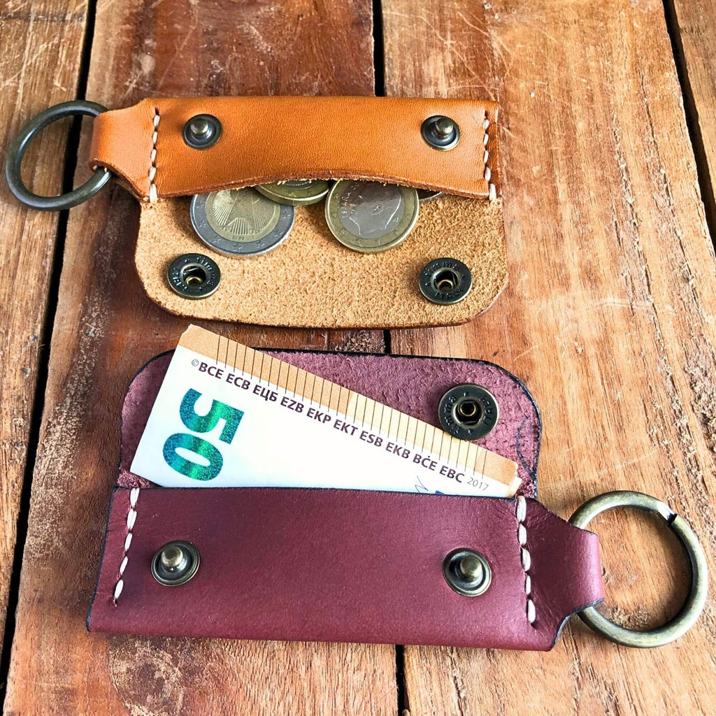 Two leather keychains wallets with coins and a banknote on a wooden surface