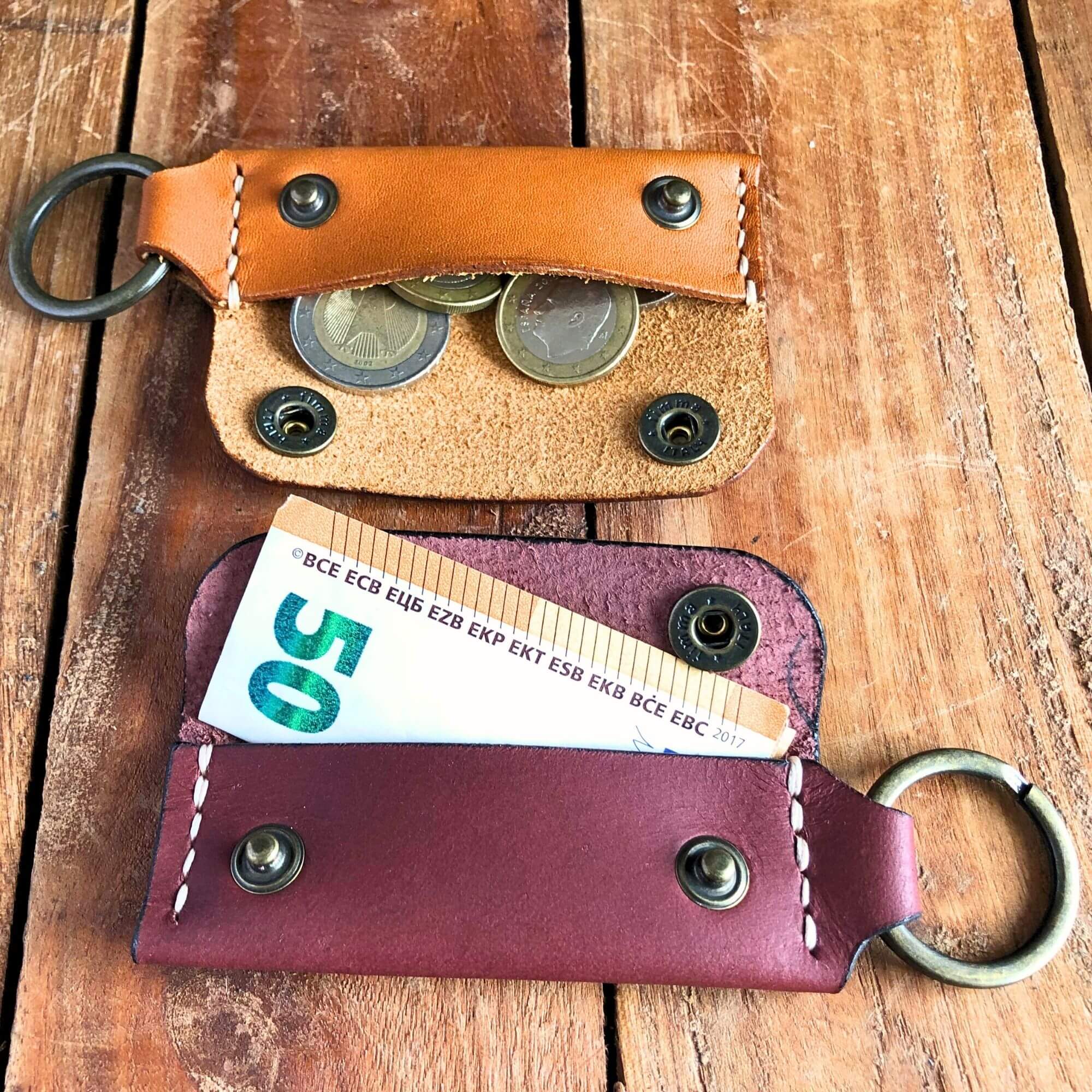Two leather keychains wallets with coins and a banknote on a wooden surface