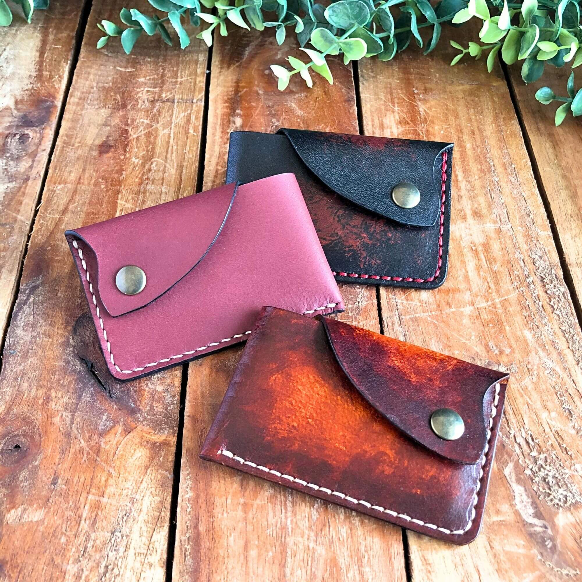 3 slim leather card wallets with snap closure on a wooden background