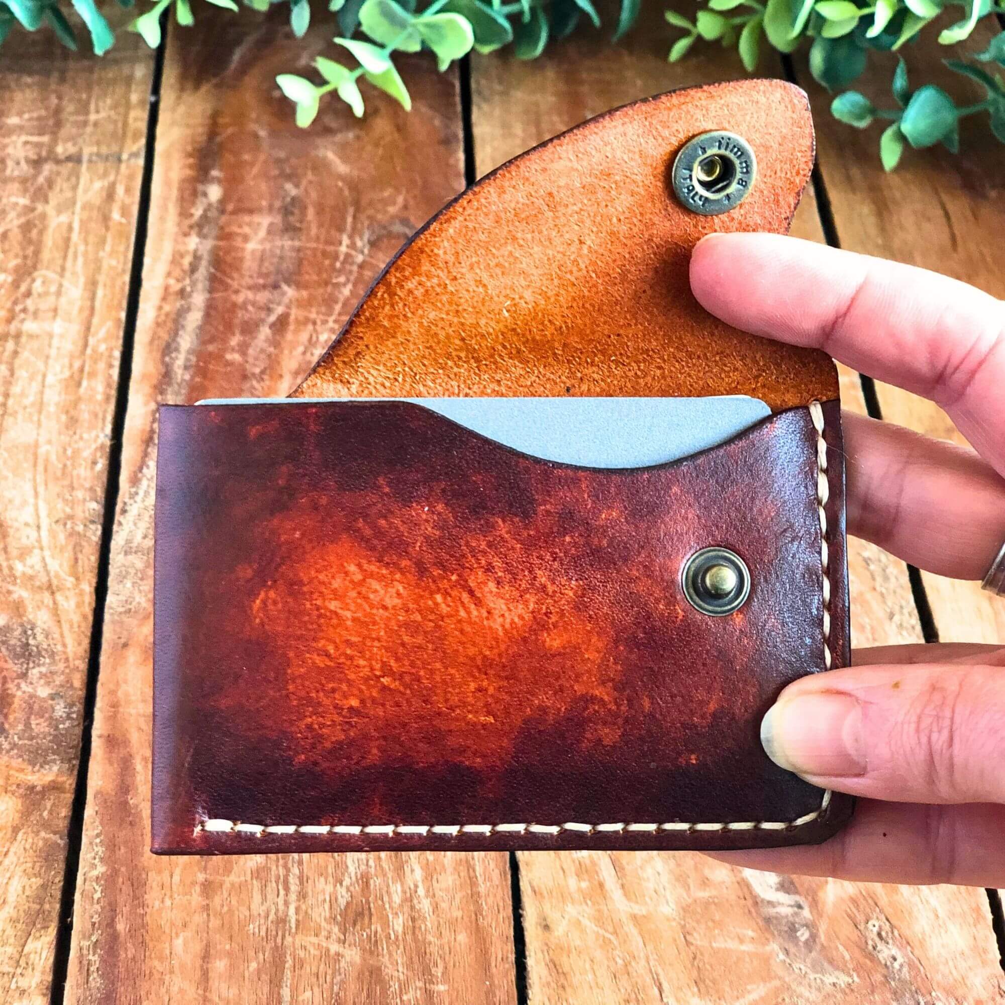 compact leather card wallet with snap closure held in hand