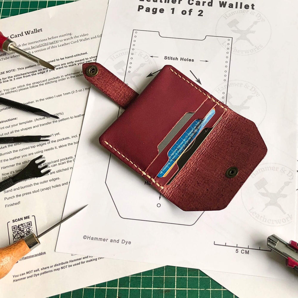 leather card wallet filled with cards laying on a printed leathercraft pattern surrounded by leathercraft tools