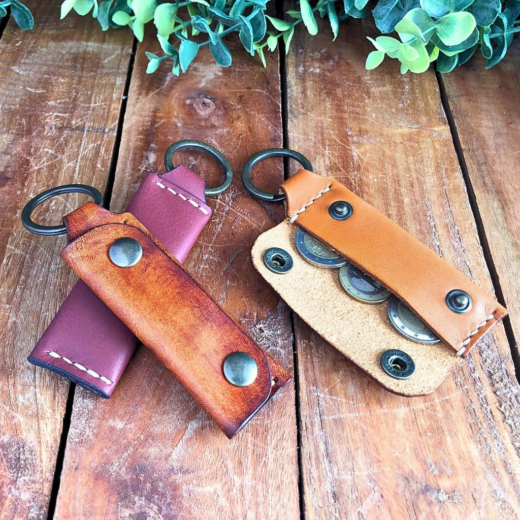 Three leather keychain wallets on a wooden surface with greenery in the background