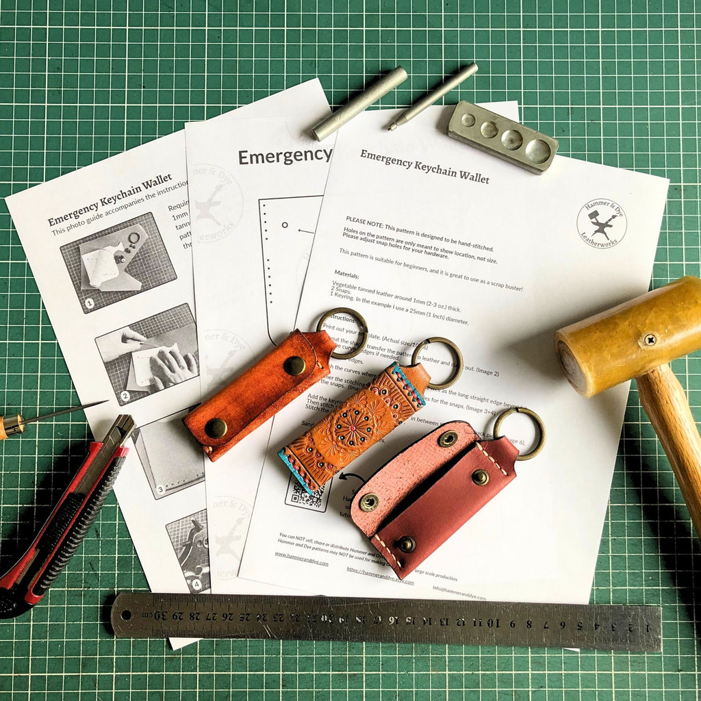 Three leather emergency keychain wallets on a printed leathercraft pattern with tools and a ruler on a green cutting mat.