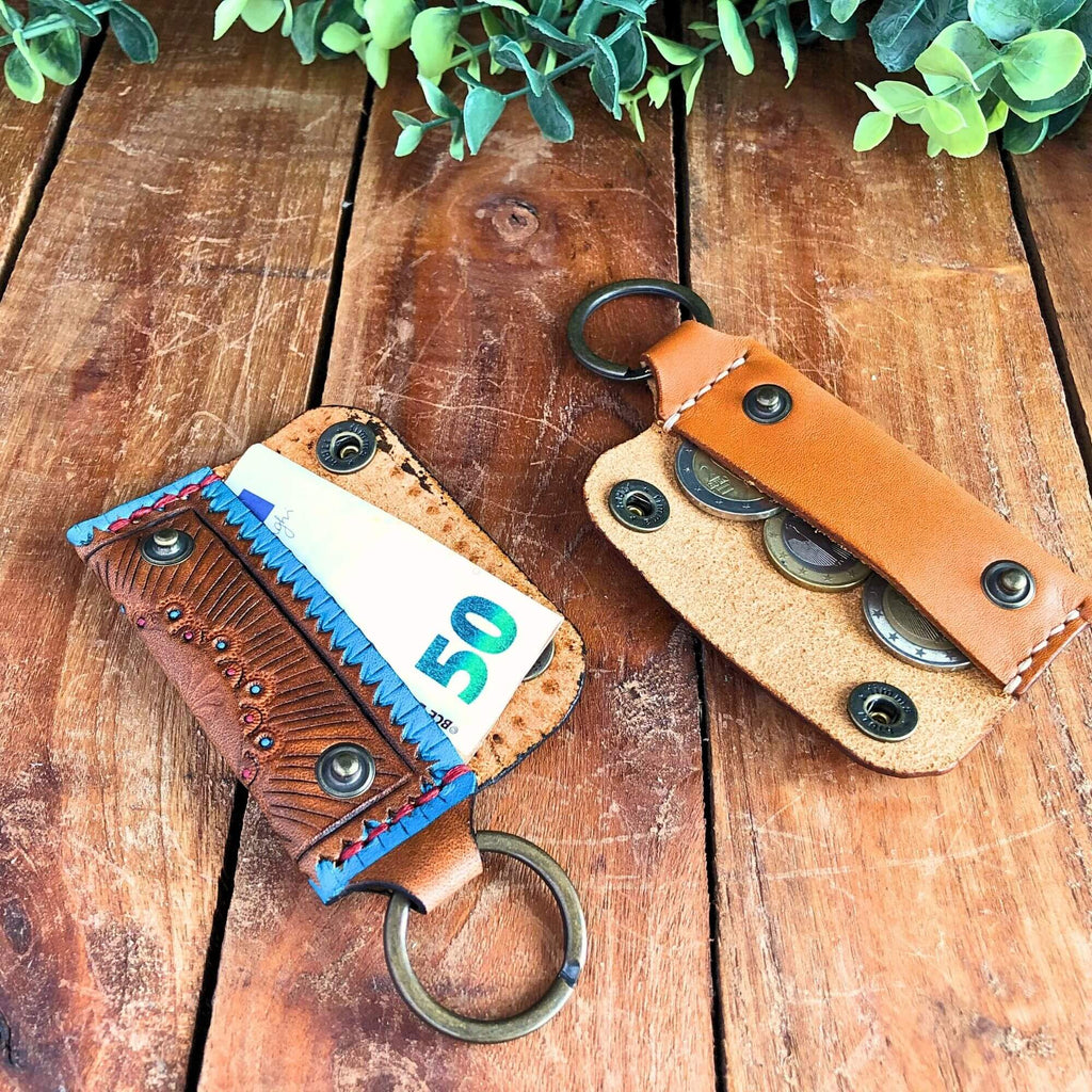 Two leather emergency keychain wallets on a wooden surface with greenery in the background