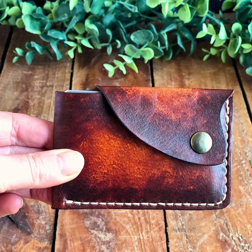minimalist leather card wallet with snap closure held in hand on a wooden surface