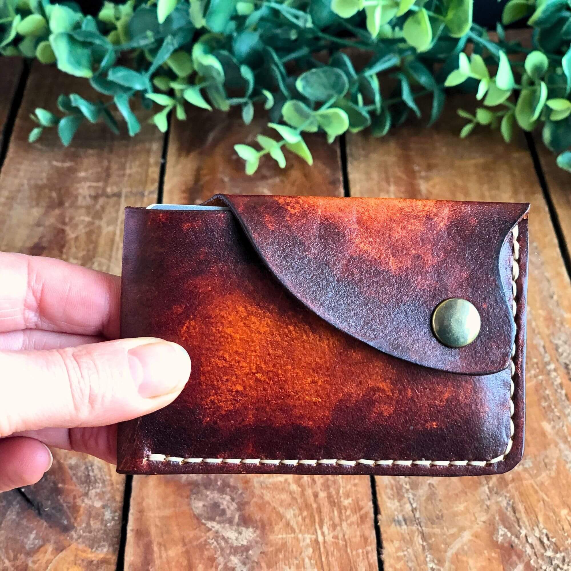 minimalist leather card wallet with snap closure held in hand on a wooden surface