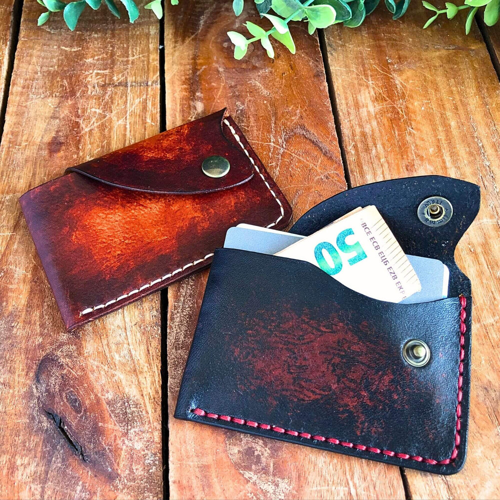 Two slim leather card wallets with snap closure on a wooden surface with one containing a 50 euro bill.