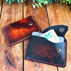 Two slim leather card wallets with snap closure on a wooden surface with one containing a 50 euro bill.