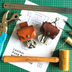 Leatherworking tools and materials on a green cutting mat with leather  dog poop pouches and a printed leathercraft pattern