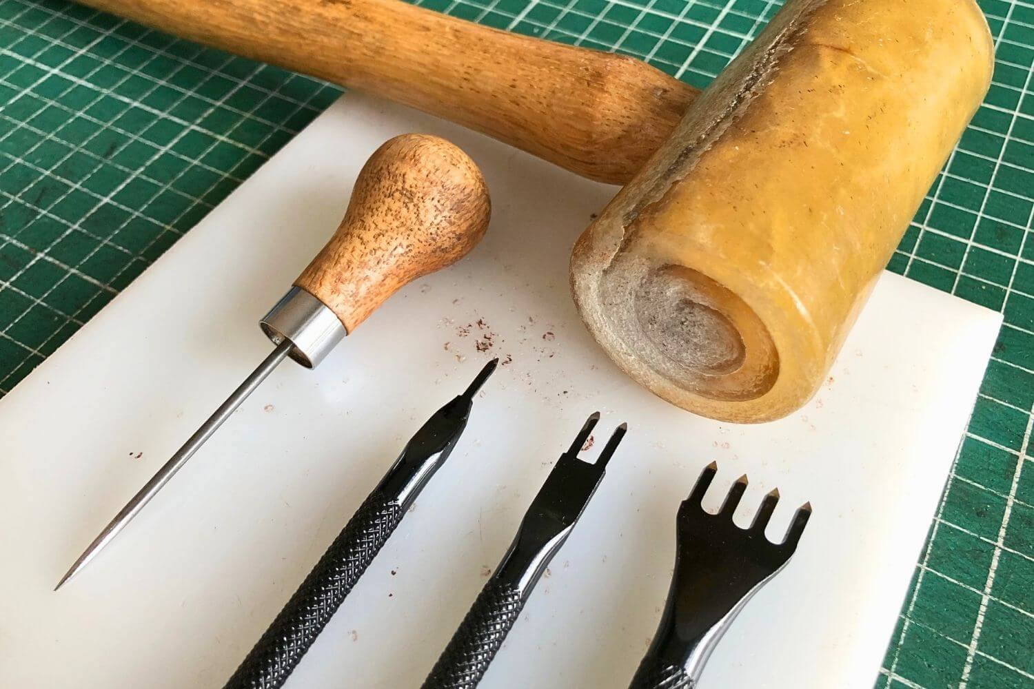 an awl, a rawhide mallet and stitching chisels on a poly board