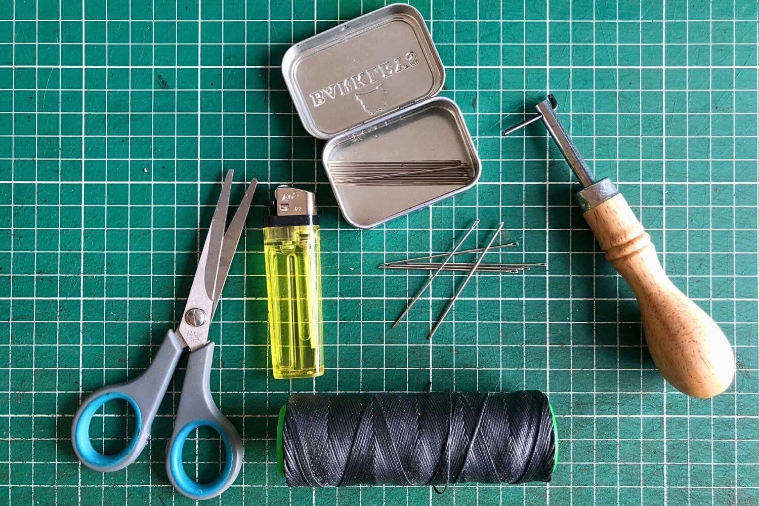 Scissors, lighter, thread and needles, and a stitch groover on a green self-healing cutting mat