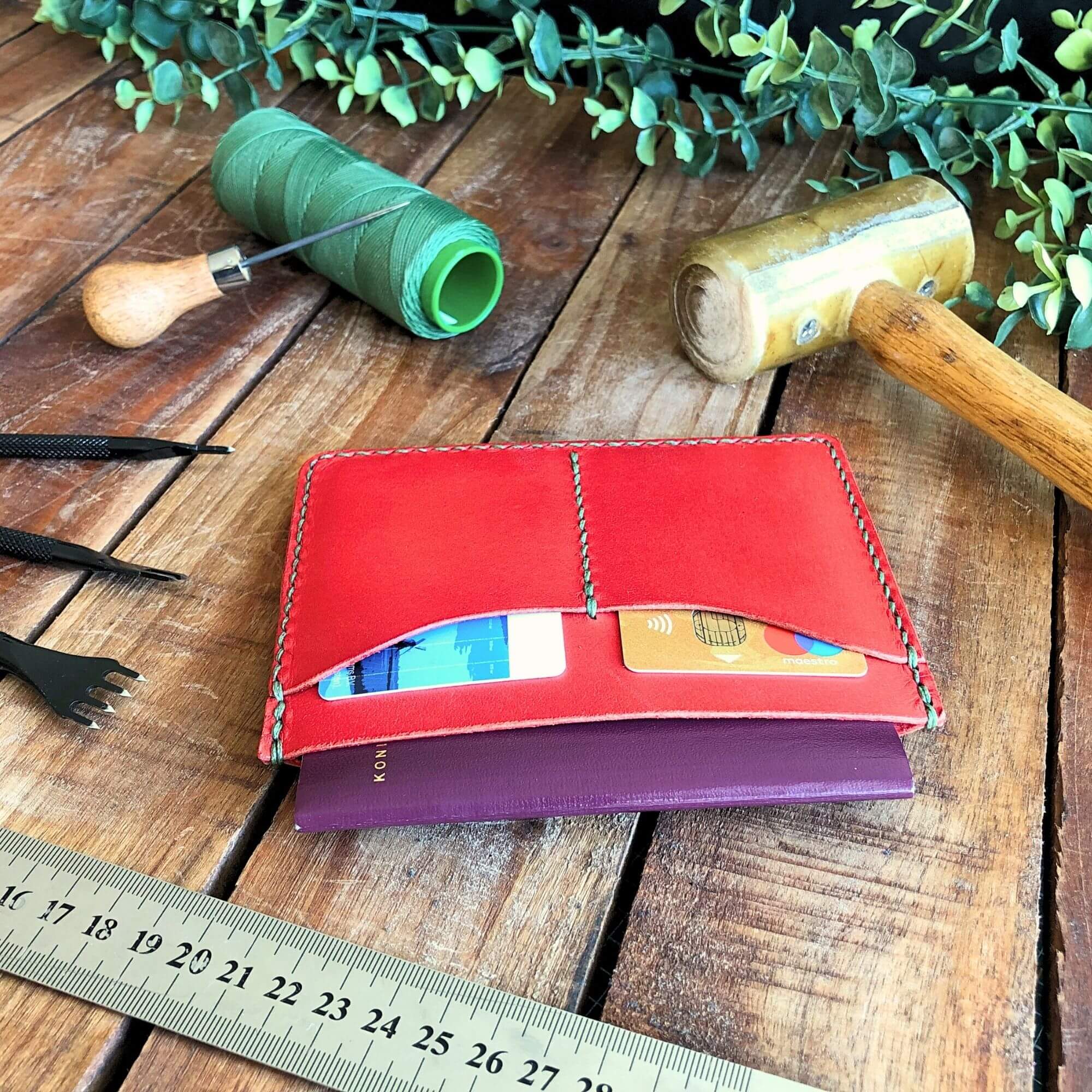 Red leather travel wallet with cards and a passport on a wooden surface with leathercraft tools
