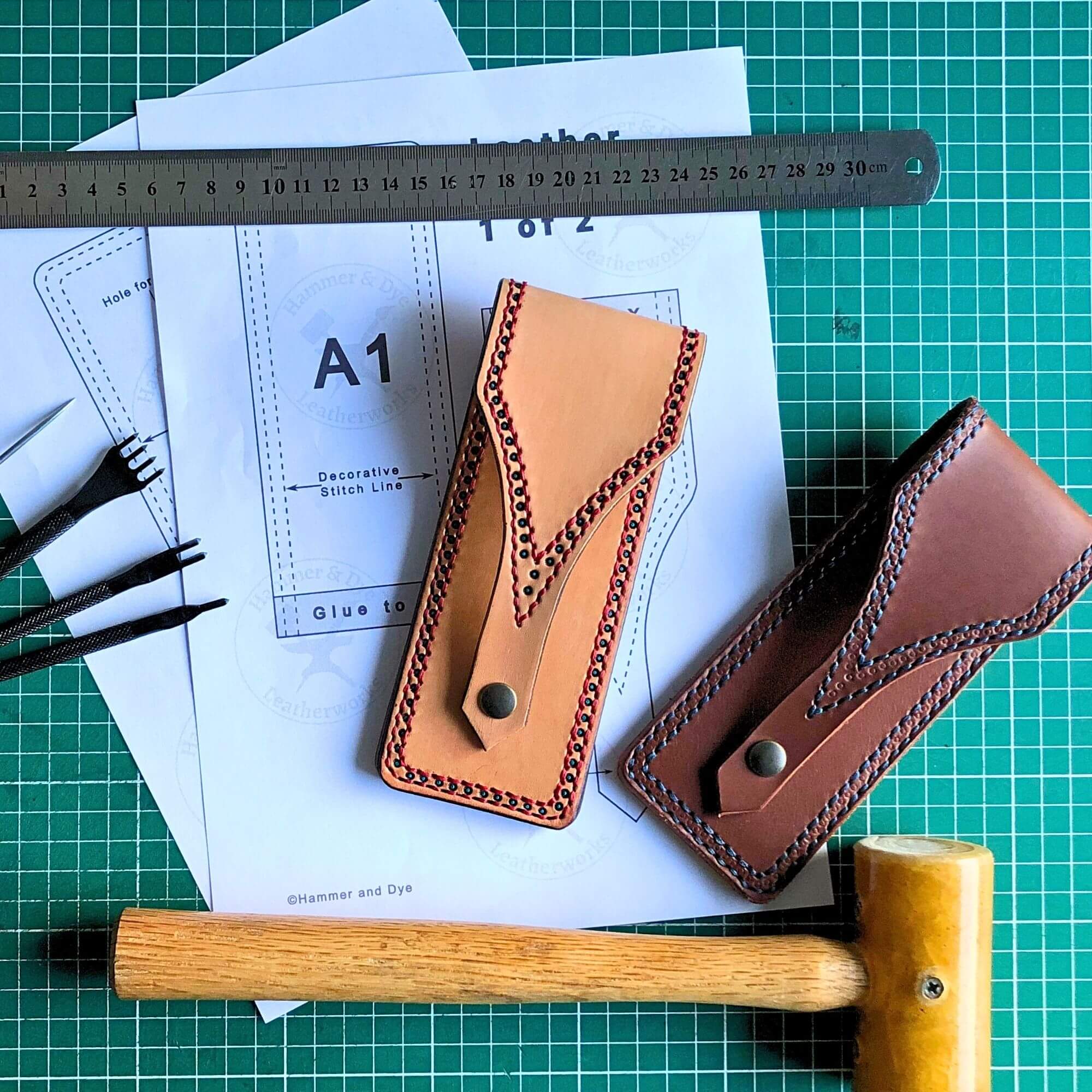 Two leather pen pouches on a cutting mat with a printed leathercraft pattern and tools.