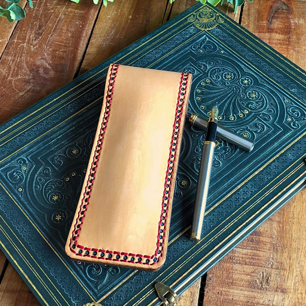 Leather pen pouch with red stitching on an ornate blue book