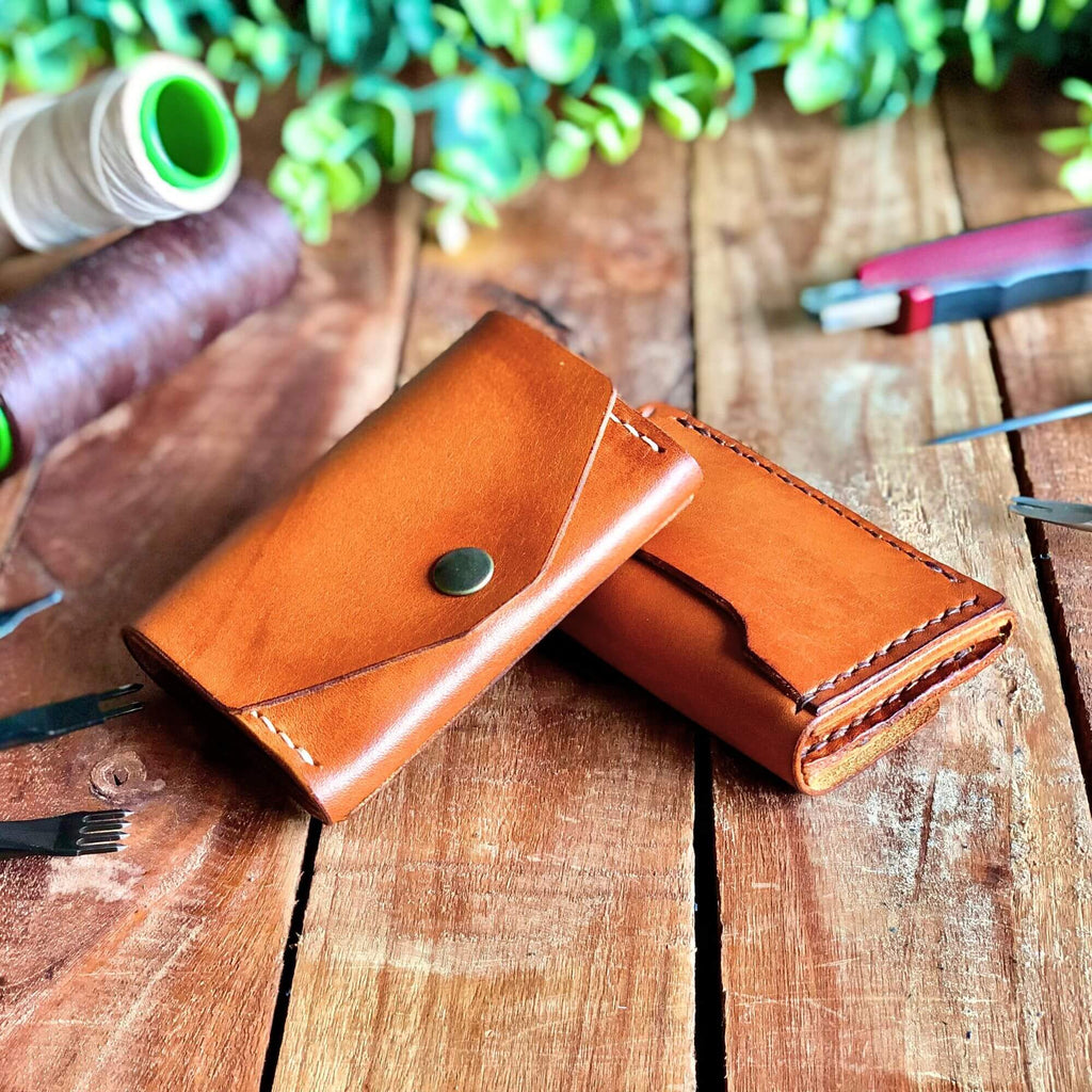 2 handcrafted leather wallets surrounded by leathercraft tools