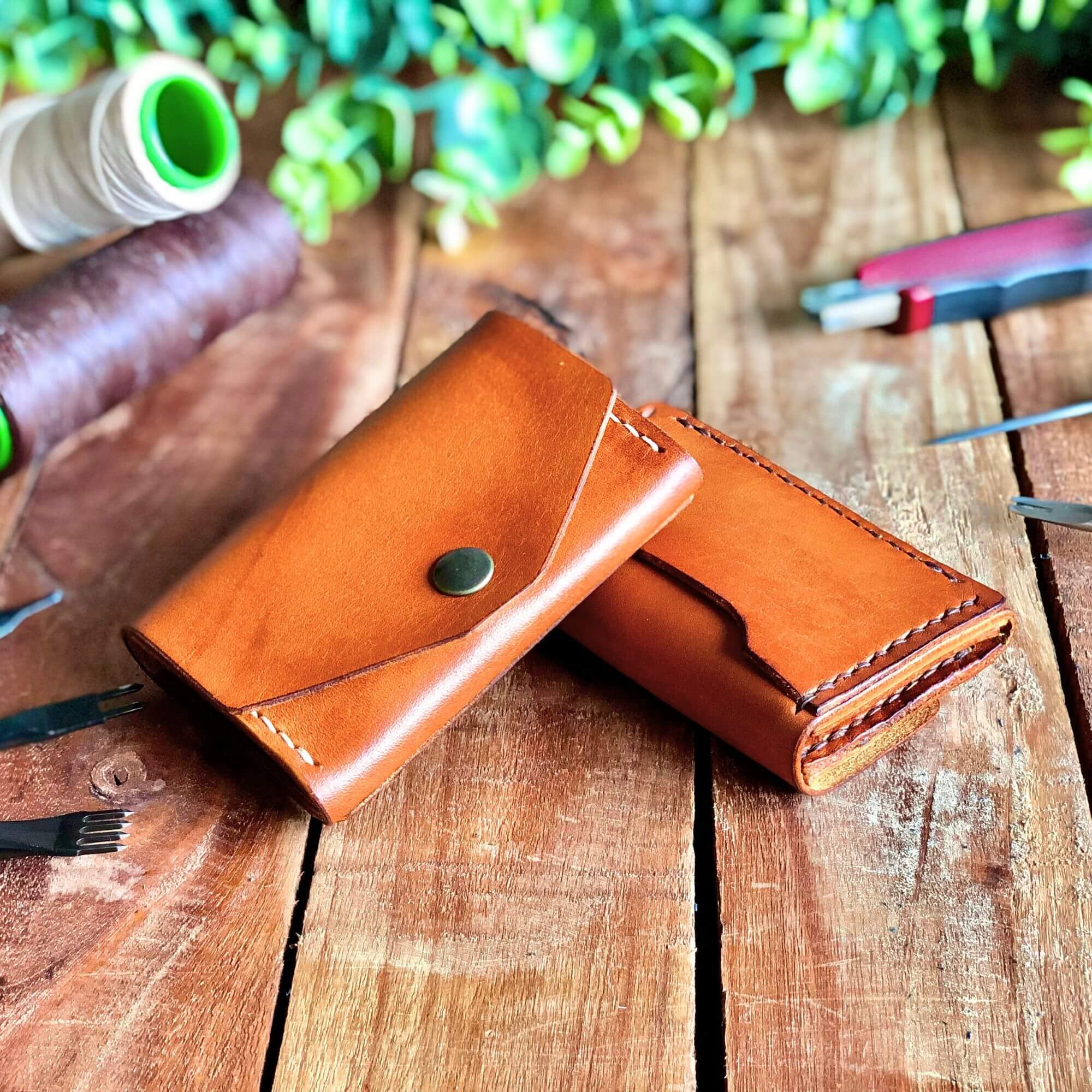 2 handcrafted leather wallets surrounded by leathercraft tools