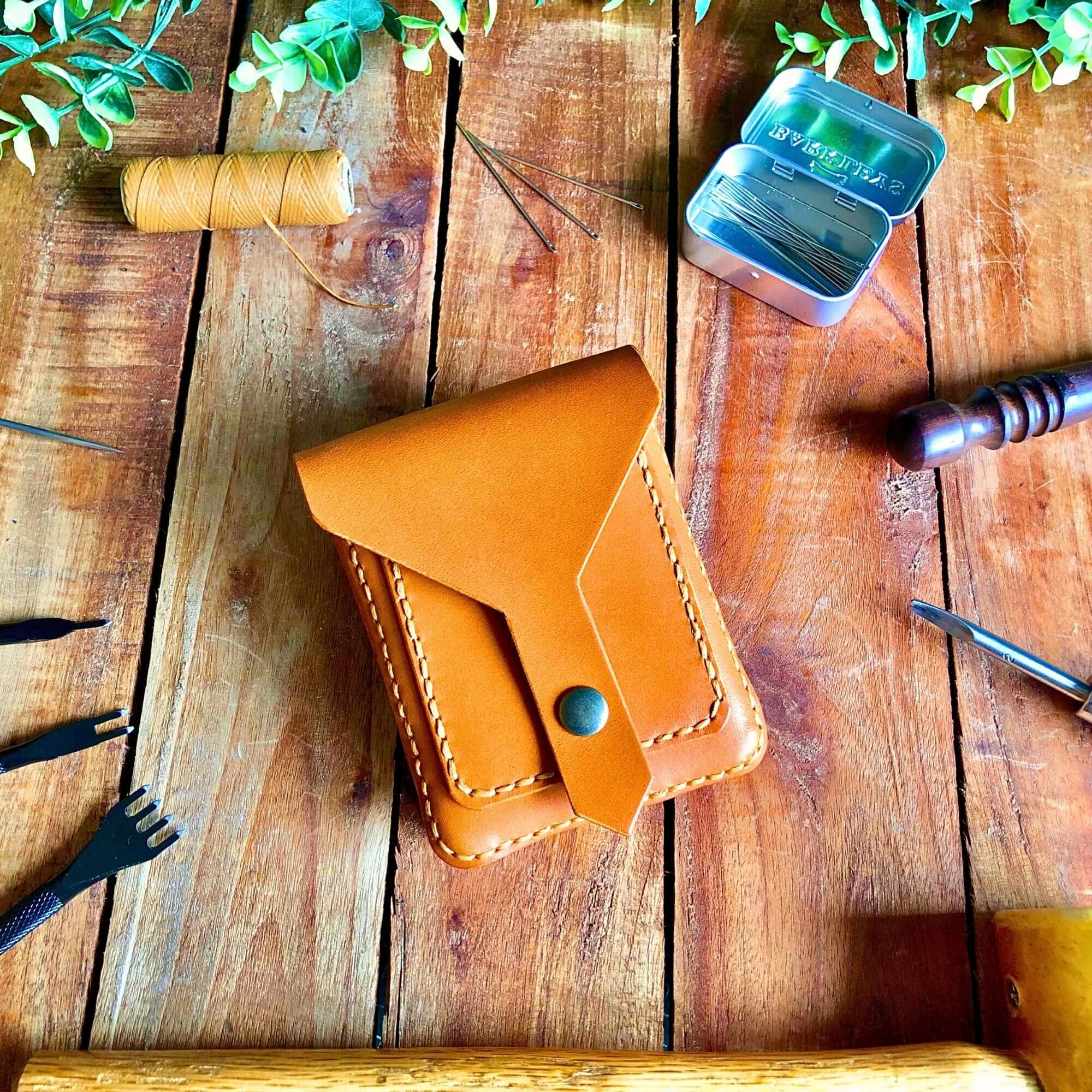 Small Tan colored belt bag surrounded by leathercraft tools on a wooden background