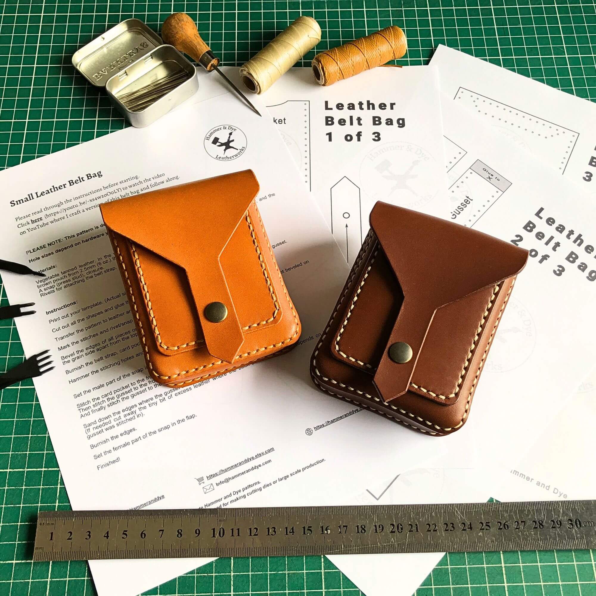 Two leather belt bags on a table with leather-making instructions and tools.