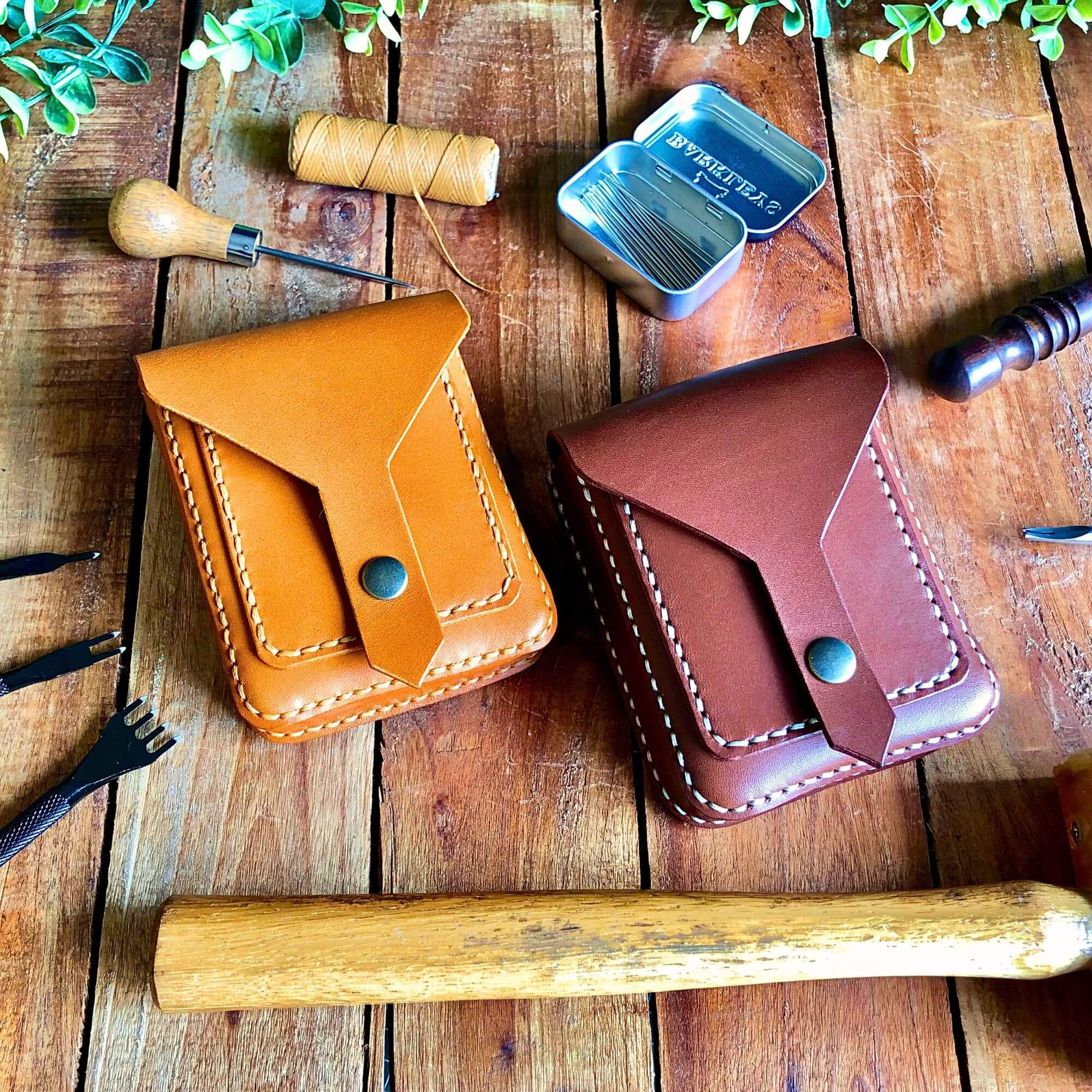 Two leather belt pouches on a wooden surface with leathercraft tools