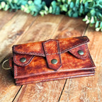 Handmade leather Dispatch Wallet on rustic wooden surface, showing front with brass snaps and D-ring