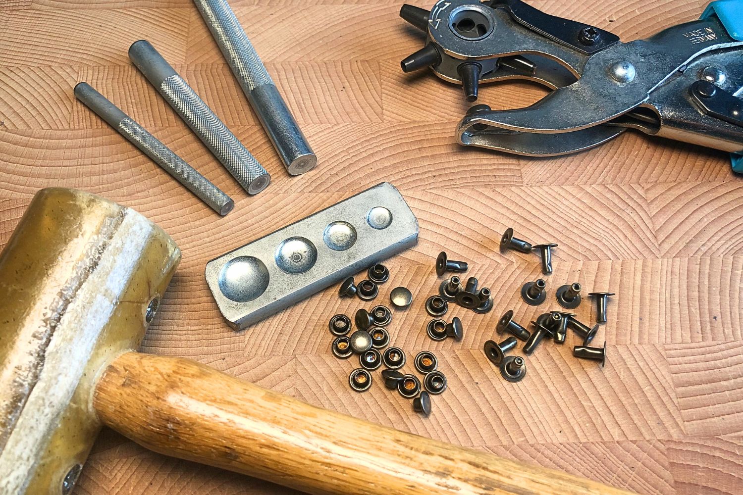rivets laid out on a wooden surface together with the tools required to install them in leather, such as a rawhide mallet and various setter tools